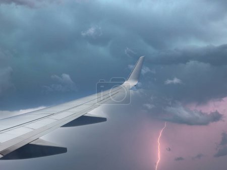 Photo for Aircraft wing slicing through thunderstorm sky, as airliner takes flight. - Royalty Free Image