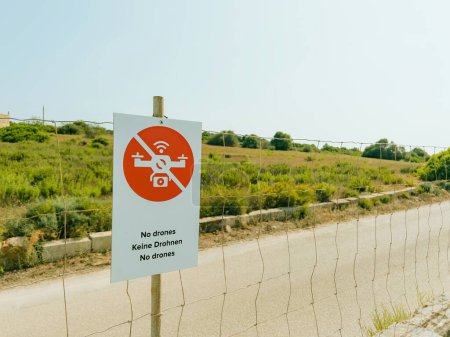 Photo for Red caution sign on fence warns of restricted area and a no-fly zone. Communication through text on sign enhances security and safety next to rural private area - no drones, keine drohnen , - Royalty Free Image