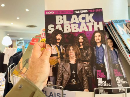 Photo for London, United Kingdom - 21 Apr 2023: POV male hand holding at press kiosk latest number of Black Sabbath Mojo british magazine featuring on the cover the worldwide known band - Royalty Free Image
