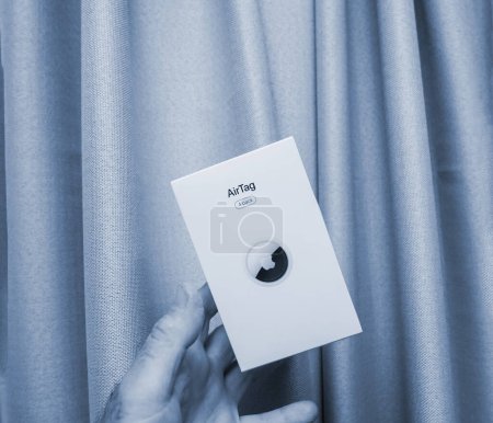 Téléchargez les photos : Paris, France - 30 mai 2023 : Homme tenant un nouveau pack Apple AirTag 4 volant au-dessus de sa main. dernier appareil par Apple pour perdu et trouvé dispositif de suivi - fond de bureau gris - en image libre de droit