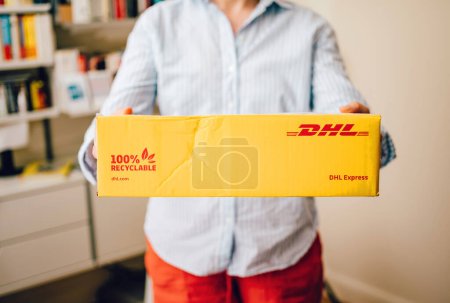 Téléchargez les photos : Hambourg, Allemagne - 11 juin 2023 : Une femme reçoit un colis DHL Express jaune avec du carton 100 % recyclable dans son salon - livraison rapide de marchandises dans le monde entier - en image libre de droit