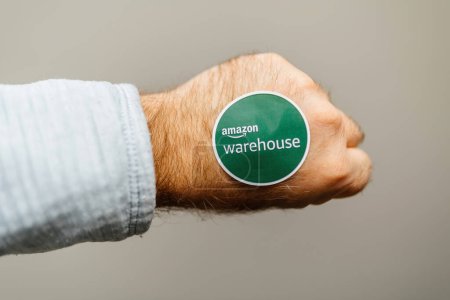 Foto de Hamburgo, Alemania - Mar 27, 2023: POV mano masculina sosteniendo verde Amazon Prime Warehouse pegado en el puñetazo de puño - fondo gris verde - Imagen libre de derechos