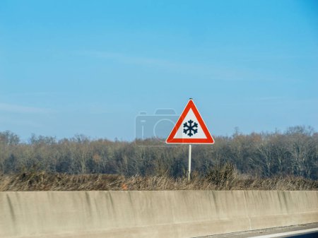 Photo for Attention-grabbing road sign on a rural highway warns of icy conditions, ensuring travel safety. No people, serene sky - snowflake in a red triangle - Royalty Free Image