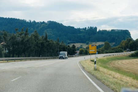 Téléchargez les photos : Schiltach, Allemagne - 14 juil. 2022 : Un paysage forestier allemand avec une route sinueuse, Mercedes-Benz van, et des panneaux routiers sous un ciel clair - en image libre de droit