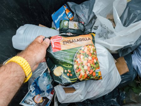 Foto de Mallorca, España - 30 de junio de 2023: Un vagabundo busca comida en un contenedor de basura para encontrar verduras congeladas nuevo pack de Findus, ensaladilla beans rebage y otras verduras - Imagen libre de derechos