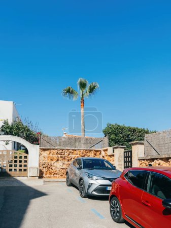Photo for Ses Covetes, Spain - Jun 26, 2023: Modern architecture in Mallorca. Blue sky and sunny weather. Toyota C-HR parked near a house. Urban living with palm trees. Ses Covetes charm. - Royalty Free Image