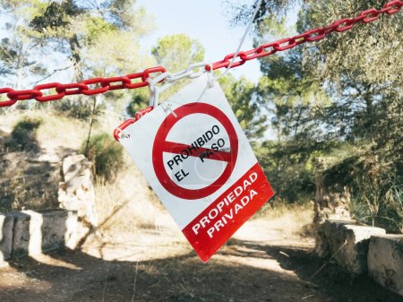 Foto de En el árbol cuelga una señal de advertencia roja que prohíbe el acceso a la propiedad privada en español, traducida como Sin entrada ilegal, propiedad privada. Ideal para proyectos de comunicación de seguridad. - Imagen libre de derechos