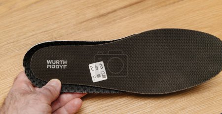 Photo for Hamburg, Germany - Feb 16, 2022: Male hand holding new Wurth Modyf protective shoe inner sole black background - wooden floor background - Royalty Free Image