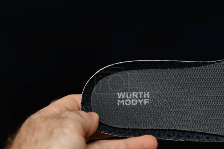 Téléchargez les photos : Hambourg, Allemagne - Feb 16, 2022 : Homme tenant une nouvelle chaussure de protection Wurth Modyf semelle intérieure fond noir - insigne de logotype visible - en image libre de droit