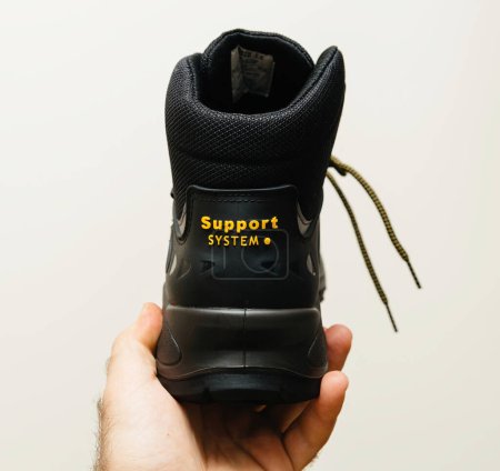 Photo for Hamburg, Germany - Feb 16, 2022: POV male hand holding new Safety shoes S3 HRO WR SRC Hydro Modytex high black - white background rear view with Support System yellow logo - Royalty Free Image