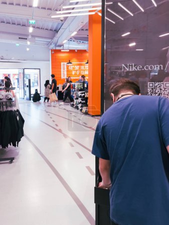 Téléchargez les photos : Roppenheim, France - 11 juillet 2023 : Vue arrière d'un employé méconnaissable du magasin Nike avec des clients qui achètent en arrière-plan de nouvelles tenues et chaussures de sport - en image libre de droit