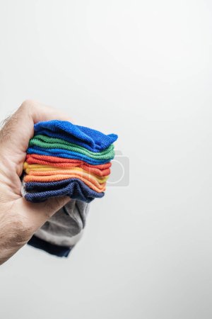 Téléchargez les photos : Main masculine berce tendrement un paquet de chaussettes vibrantes, méticuleusement organisées, chaque couleur soigneusement désigné pour un jour de la semaine - en image libre de droit