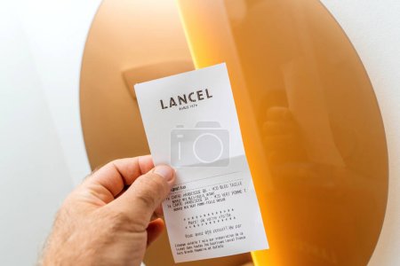 Téléchargez les photos : Paris, France - 25 août 2023 : Une main masculine POV tenant un reçu du magasin de mode Lancel contre le miroir doré - en image libre de droit