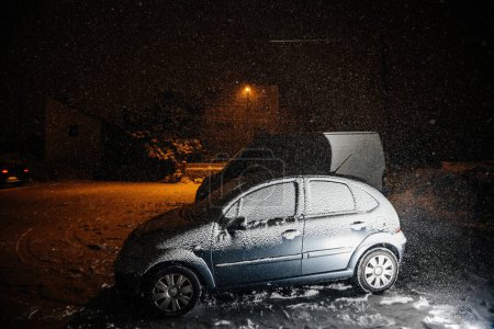 Foto de Estrasburgo, Francia - 18 de diciembre de 2022: Un Citroen cubierto de nieve estacionado en una calle nevada cerca de un campo en una noche nevada, mostrando el transporte en condiciones climáticas desafiantes durante la tormenta de nieve - Imagen libre de derechos