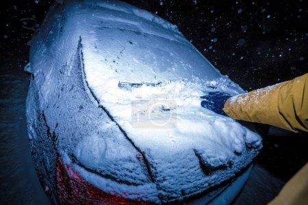 Foto de Un hombre quitando diligentemente la nieve de un coche durante una noche amargamente fría en medio de una tormenta de nieve. - Imagen libre de derechos