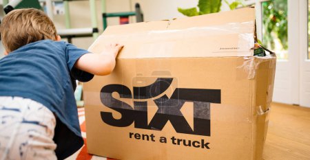 Photo for Bremen, Germany - Aug 14, 2023: A toddler hand on the box in a living room, pointing to sixt rent a truck cardboard boxes. They are getting ready to move to a new house or apartment. The view is from - Royalty Free Image