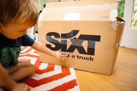 Photo for Bremen, Germany - Aug 14, 2023: A young child points to sixt Rent a Truck cardboard boxes in a well-lit living room, signaling a move to a new home - Royalty Free Image