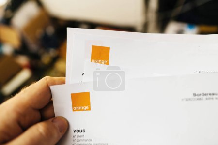 Téléchargez les photos : Paris, France - 27 mars 2023 : Une perspective à la première personne montre un homme tenant une facture en papier Orange Telecom ornée du logo carré distinctif - en image libre de droit