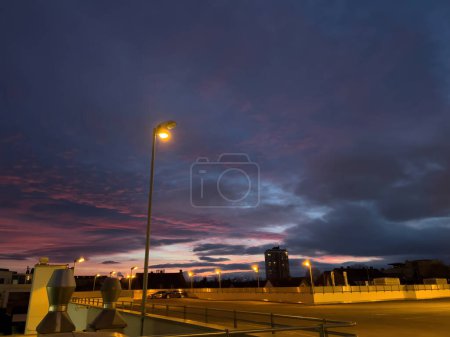 Photo for Architecture, city at dusk, illuminated structure, empty roof parking, street lights, sunset sky with clouds. Nighttime urban scene. - Royalty Free Image