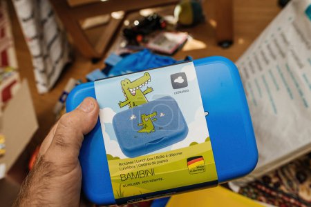 Photo for Paris, France - Sep 2, 2023: male hand grasps the Leonardo plastic lunchbox, featuring a crocodile on the cover. Its "Made in Germany" label and "Bambini series" branding emphasize both quality and - Royalty Free Image