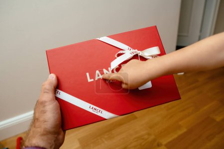 Photo for Paris, France - Aug 25, 2023: A toddler excitedly points out the Lancel logo on a gift box to an adult. - Royalty Free Image