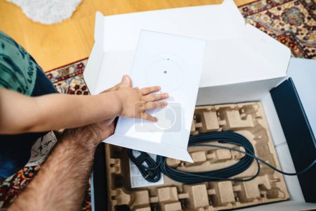 Photo for Bremen, Germany - Aug 14, 2023: A toddler places his hand on the router of a SpaceX Starlink internet satellite kit during unboxing, with his father guiding him through the process. - Royalty Free Image