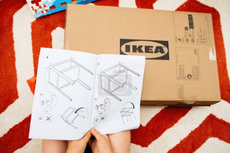 Téléchargez les photos : Paris, France - 29 juil. 2023 : Les tout-petits POV : Saisir les instructions de IKEA Knarrevik sur la table de nuit, sur le point d'assembler de nouveaux meubles suédois. - en image libre de droit