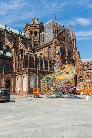 Téléchargez les photos : Strasbourg, France - 7 juil.2023 : Cathédrale Notre-Dame de Strasbourg, des piétons défilent tandis que des ouvriers dévoués travaillent avec diligence pour installer une structure artistique intrigante. - en image libre de droit