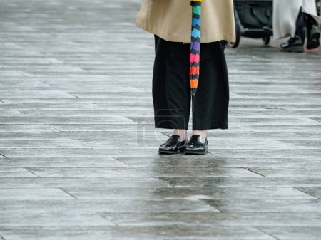 Foto de Contra un suave telón de fondo bokeh, una mujer anónima se levanta de frente, elegantemente vestida con una gabardina mientras sostiene un paraguas - Imagen libre de derechos