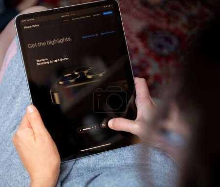 Foto de Londres, Reino Unido - Sep 13, 2023: mujer en su sala de estar lee el sitio web de Apple Computers, explorando el último teléfono inteligente iPhone 15 Pro, conocido por su caja de titanio. - Imagen libre de derechos