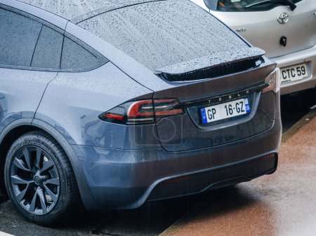 Téléchargez les photos : Neufchatel-Hardelot, France - 18 août 2023 : Par le haut, la partie arrière d'une nouvelle voiture électrique Tesla Model X navigue sous de fortes pluies, avec une multitude de gouttes de pluie - en image libre de droit