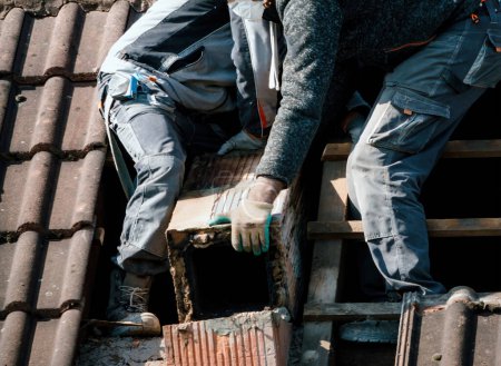 Téléchargez les photos : Des travailleurs masculins dévoués sur le toit démontent méticuleusement une cheminée en brique lors d'un projet complet de rénovation domiciliaire. - en image libre de droit