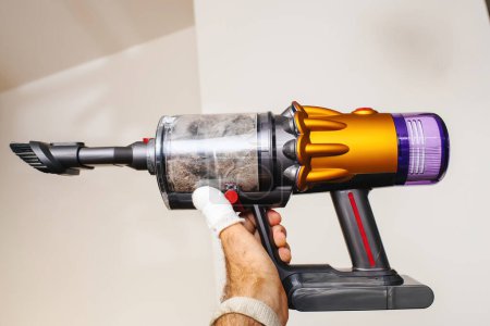 Photo for Despite an injured hand concealed by bandages, a determined individual confidently wields a cordless vacuum against the interior walls of a house - Royalty Free Image