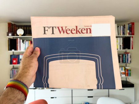 Photo for Paris, France - Sep 18, 2023: Man holds latest FT Weekend with front-page advertising, while Vitsoe shelves are visible in the background, merging news and modern design elements. - Royalty Free Image
