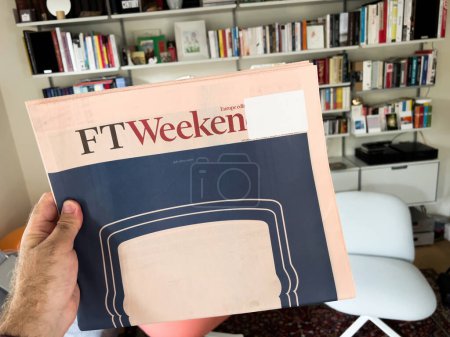 Photo for Paris, France - Sep 18, 2023: A man holds the latest FT Weekend with large cover advertising, while Vitsoe shelves are visible in the background, blending news and modern design - Royalty Free Image