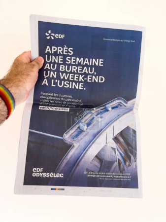 Téléchargez les photos : Paris, France - 18 sept. 2023 : Une main humaine tient une page publicitaire Le Monde d'EDF Energy Company, invitant le public à visiter ses installations lors du Journee du Patrimoine annuel - en image libre de droit