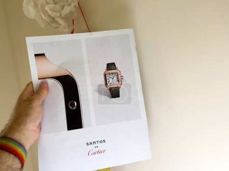 Foto de París, Francia - 18 de septiembre de 2023: Se captura una mano de hombre sosteniendo una revista de lujo, abierta a una página de publicidad que muestra un reloj Santos de Cartier - Imagen libre de derechos