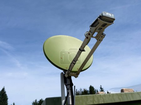 Téléchargez les photos : Une antenne parabolique, peinte en vert camouflage, est visible contre un ciel bleu sur un site militaire, indiquant son emplacement stratégique pour des opérations secrètes - en image libre de droit