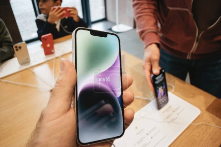 Photo for Paris, France - Sep 22, 2022: A male hand is seen holding the latest Apple iPhone 14, while other customers peruse various phones in the background during the devices launch day. - Royalty Free Image