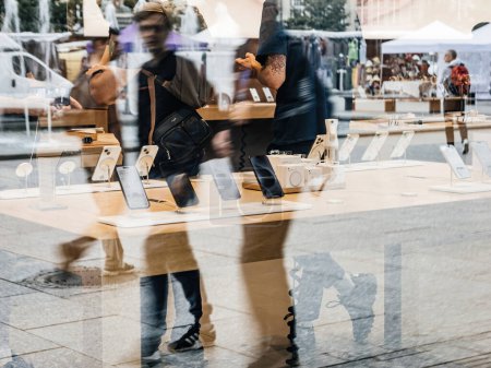 Téléchargez les photos : Paris, France - 22 sept. 2023 : Capturées à partir d'un point de vue extérieur, des silhouettes d'individus traversent les environs d'un Apple Store, où les iPhone 15 Pro et Max sont bien en évidence sur - en image libre de droit