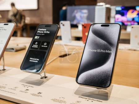 Photo for Paris, France - Sep 22, 2023: A row of the newly-released titanium iPhone 15 Pro smartphones by Apple Computers is displayed inside an Apple Store, with customers actively shopping in the background - Royalty Free Image