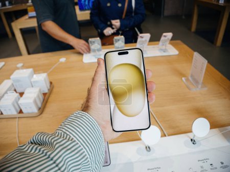Foto de París, Francia - 22 de septiembre de 2023: POV masculino, el último teléfono inteligente iPhone 15 se sostiene en la mano dentro de una tienda de Apple, como una pareja en el fondo delibera sobre qué modelo comprar - Imagen libre de derechos