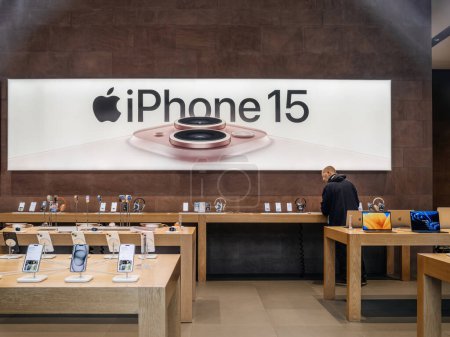 Téléchargez les photos : Paris, France - 22 sept. 2023 : Apple Store avec le lancement de la série iPhone 15, un client solitaire est vu englouti dans les smartphones, sur fond de grande bannière avec l'iPhone 15 sur - en image libre de droit