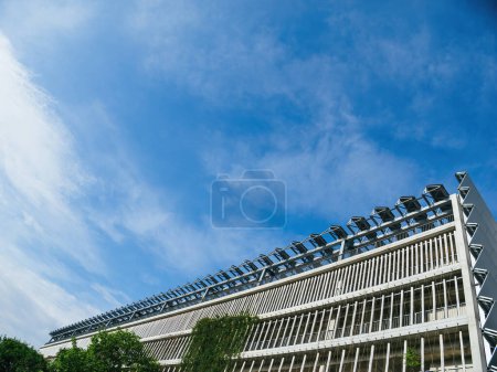 Téléchargez les photos : Capturée sous un angle bas, une centrale solaire se trouve au sommet d'un grand parking public, face à un ciel bleu clair. - en image libre de droit