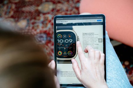 Foto de Londres, Reino Unido - 13 de septiembre de 2023: Mujer leyendo sobre el último Apple Watch Ultra 2 en Apple.com a través de su iPad, con el sitio web con especificaciones detalladas y botón de acción en naranja internacional. - Imagen libre de derechos
