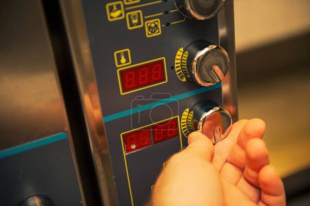 Photo for Close-up of a male chefs hand turning the control knob on a professional oven in a restaurant kitchen - Royalty Free Image