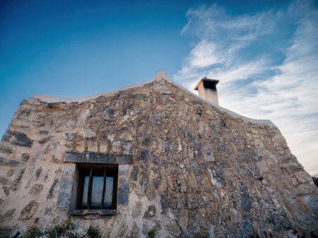 Téléchargez les photos : Capturée sous un angle bas, une maison de pêcheurs en pierre méticuleusement construite se dresse sur fond de ciel bleu vif, créant une scène cinématographique frappante - en image libre de droit