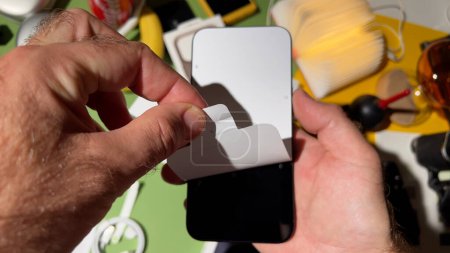Foto de Londres, Reino Unido - 25 de septiembre de 2023: Hombre pelando cuidadosamente la lámina de papel de protección de la pantalla OLED Retina del nuevo iPhone 15 Pro Max - Imagen libre de derechos