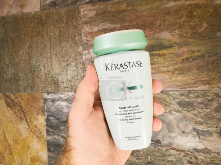 Photo for London, UK - Sep 28, 2023: A male hand holds a new bottle of Kerastase Paris Volumifique thickening effect shampoo for fine hair in a luxury bathroom setting. - Royalty Free Image