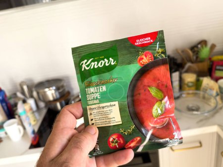 Photo for London, UK - Sep 28, 2023: A male hand holds a package of Knorrs Tomaten Suppe, a delicious instant tomato soup, in a kitchen environment. - Royalty Free Image